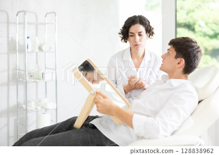 Young man having consultation about face aesthetic while looking in the mirror 128838962