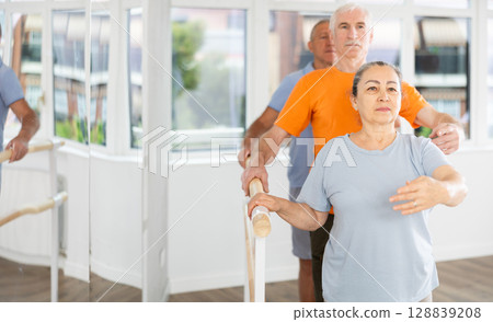 Group of elderly women and men practice ballet moves in classical dance school 128839208