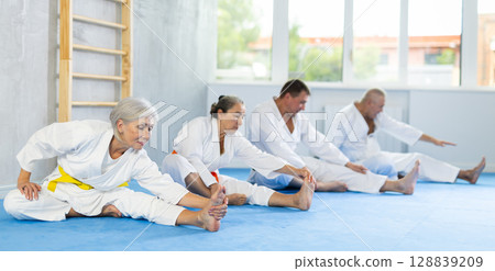 Old woman wearing kimono practicing leg stretching position in sports hall 128839209