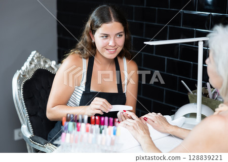 Girl manicurist works with unrecognizable pensioner client, files nails and performs hand care Girl manicurist works with unrecognizable pensioner client, files nails and performs hand care 128839221