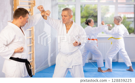 Old man attendee of karate classes fighting with his opponent in sports hall 128839225