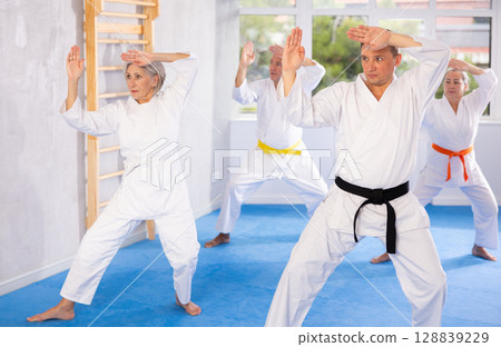 Middle-aged man attendee of karate classes practicing kata standing in row with others 128839229