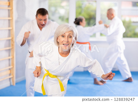 Group of mature people in kimono sparring together in gym during karate training 128839247