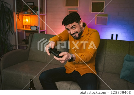 Excitement fills the room as a man immerses himself in an intense video game session during a cozy evening at home 128839408