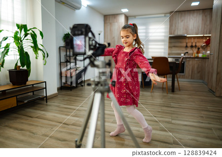 Girl performing a dance routine in a cozy living room while being filmed for a creative project during daylight hours Girl performing a dance routine in a cozy living room while being filmed for a creative project during daylight hours 128839424