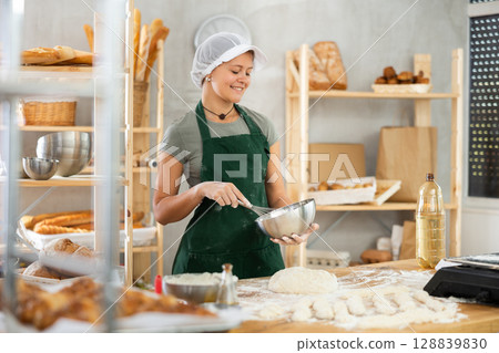 Female bkery cook whisks chicken eggs to make dough in bakery kitchen 128839830