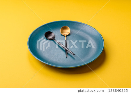 Empty plate with devices in the form of clock hands as a conceptual background for lunch time Empty plate with devices in the form of clock hands as a conceptual background for lunch time 128840235