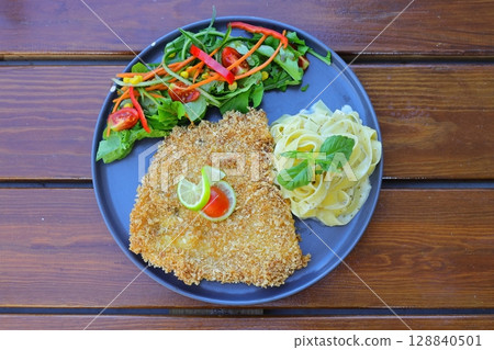 Chicken schnitzel with salad and pasta on the wooden background. With white wine. Chicken schnitzel with salad and pasta on the wooden background. With white wine. 128840501