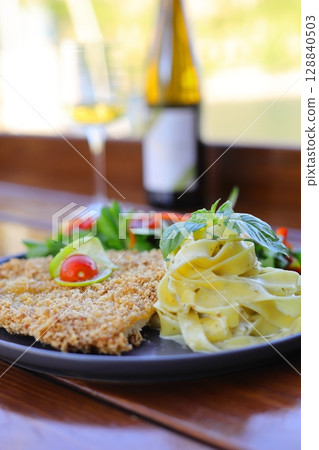 Chicken schnitzel with salad and pasta on the wooden background. With white wine. Chicken schnitzel with salad and pasta on the wooden background. With white wine. 128840503