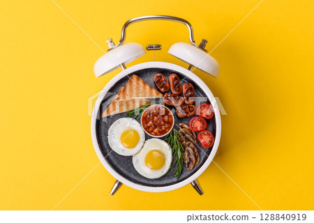 Breakfast of fried eggs with bacon or sausage and vegetables. ? plate on a vintage alarm clock Breakfast of fried eggs with bacon or sausage and vegetables. ? plate on a vintage alarm clock 128840919