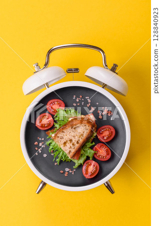 Breakfast sandwich with toast, avocado and tomatoes. Breakfast as a plate concept on a alarm clock 128840923