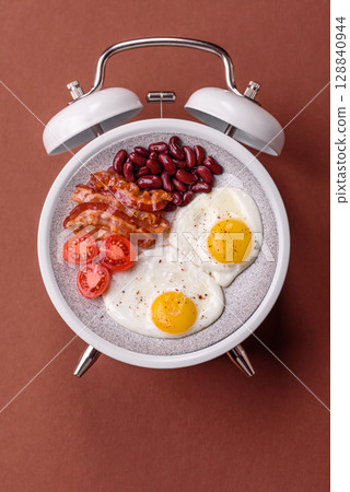 Breakfast of fried eggs with bacon or sausage and vegetables. ? plate on a vintage alarm clock 128840944