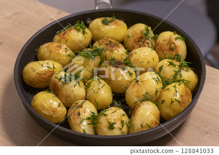 Young jacket potatoes fried in a frying pan and sprinkled with herbs Young jacket potatoes fried in a frying pan and sprinkled with herbs 128841033