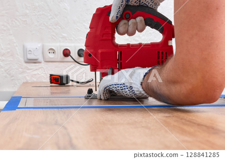 repairman with electric jigsaw doing sawing place for installing hob in a worktop in the kitchen, close-up 128841285