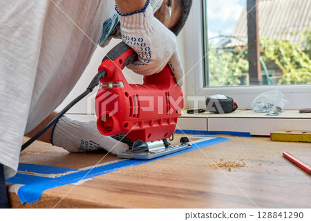 repairman using handheld electric jigsaw and cutting hole for the sink in the kitchen countertops repairman using handheld electric jigsaw and cutting hole for the sink in the kitchen countertops 128841290
