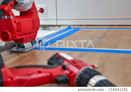 repairman using electric jigsaw and cutting hole for the sink in the kitchen countertops 128841292
