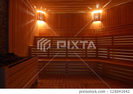Seat in sauna room. Empty wooden steam room with stone heater.Sauna room for good health. Seat in sauna room. Empty wooden steam room with stone heater.Sauna room for good health. 128841642