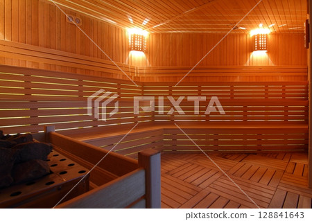 Seat in sauna room. Empty wooden steam room with stone heater.Sauna room for good health. Seat in sauna room. Empty wooden steam room with stone heater.Sauna room for good health. 128841643