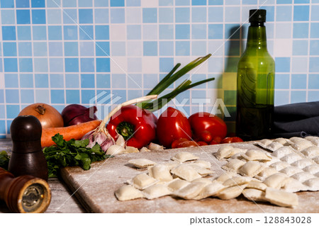 Fresh ravioli with flour on wooden cutting board with vegetables and spices 128843028