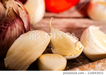Fresh garlic bulb and cloves resting on rustic wooden table 128843032