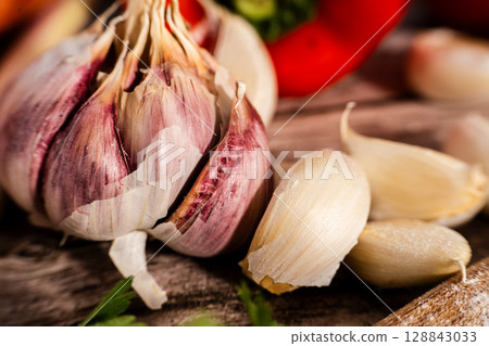 Fresh garlic bulb and cloves resting on rustic wooden table Fresh garlic bulb and cloves resting on rustic wooden table 128843033