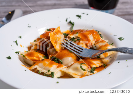 Fork lifting ravioli with tomato sauce from white plate Fork lifting ravioli with tomato sauce from white plate 128843050