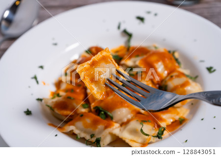 Fork lifting ravioli with tomato sauce from white plate Fork lifting ravioli with tomato sauce from white plate 128843051