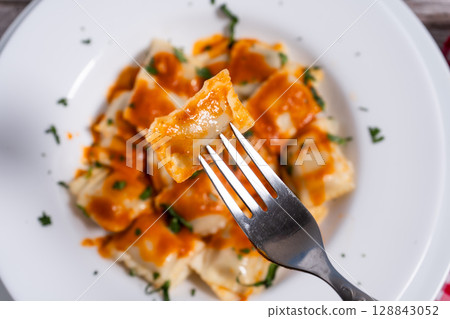 Fork lifting ravioli with tomato sauce from white plate Fork lifting ravioli with tomato sauce from white plate 128843052