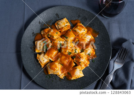 Ravioli pasta with tomato sauce and parsley topping on elegant dark plate Ravioli pasta with tomato sauce and parsley topping on elegant dark plate 128843063