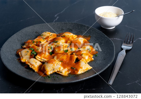 Ravioli pasta with tomato sauce and grated cheese on dark plate 128843072