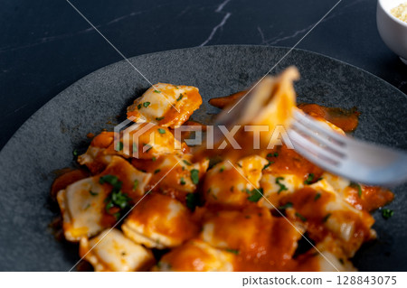 Ravioli pasta with tomato sauce and parsley topping on elegant dark grey plate 128843075