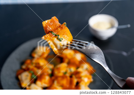 Fork lifting ravioli with tomato sauce and parsley garnish 128843077