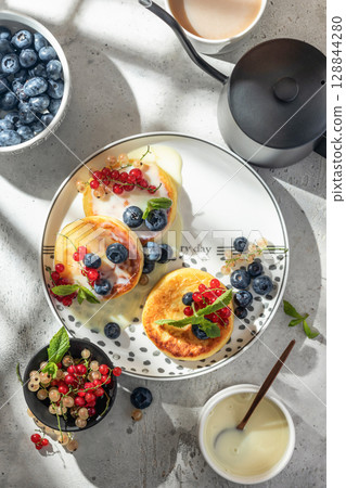 Cottage cheese pancakes with berries and condensed milk top view. Homemade dessert syrniki for healthy breakfast, bright morning light Cottage cheese pancakes with berries and condensed milk top view. Homemade dessert syrniki for healthy breakfast, bright morning light 128844280