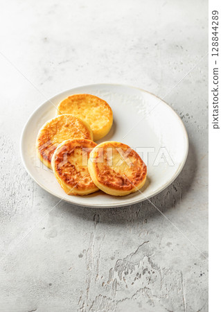 Cottage cheese pancakes on a plate on light background isolated. Homemade dessert syrniki for healthy breakfast, text space 128844289