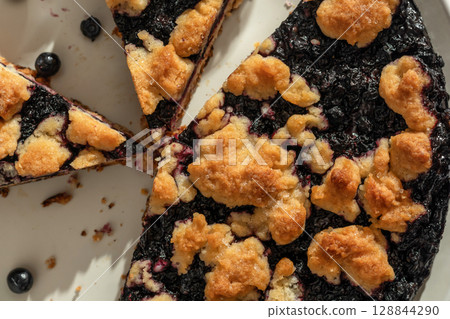 Sliced homemade blueberry crumble pie on a plate close up top view. Sweet breakfast composition in bright morning light 128844290