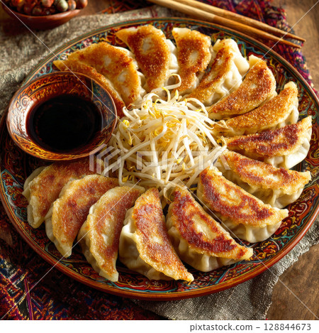 platter of crispy pan-fried gyoza dumplings, accompanied by a small bowl of soy sauce and a mound of fresh bean sprouts. Themes of delicious, traditional Asian cuisine, perfect for a meal or appetizer 128844673