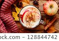Top view cozy autumn drink with spices, apples, and wool scarf in warm light on rustic wood surface 128844742