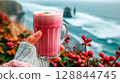 Hand holding pink beetroot matcha latte with creamy foam, coastal morning vibe 128844745