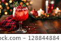 Burgundy mocktail in wine glass with pomegranate and rosemary on dark wood, plaid scarf and candlelight behind 128844884