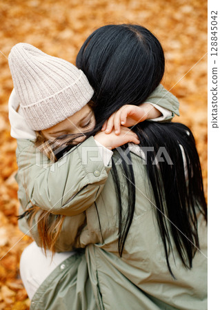 Woman and her little girl playing in autumn forest and laughing. Brunette man hugging her daughter. Family wearing green coats. 128845042