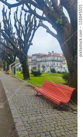 A peaceful waterfront with red benches under moss-covered trees, overlooking the pier in the town of Viana do Castelo in Portugal. The ideal concept of urban nature, with leisure, travel, 128845055