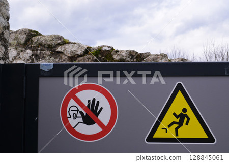 Industrial safety signage on a gray fence wall, including a no entry symbol and a falling hazard warning. Concept of danger, security, and workplace caution. 128845061