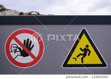 Industrial safety signage on a gray fence wall, including a no entry symbol and a falling hazard warning. Concept of danger, security, and workplace caution. 128845062