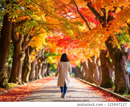 一位女士沿著綠樹成蔭、落滿秋葉的小路行走 128847127