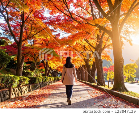 一位女士沿著綠樹成蔭、落滿秋葉的小路行走 128847129