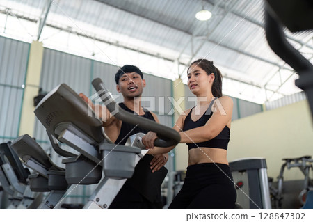 Trainer guiding female athlete on exercise equipment Trainer guiding female athlete on exercise equipment 128847302