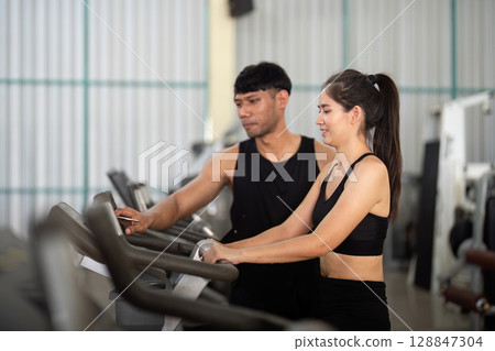 Trainer and woman engaging in workout at gym equipment Trainer and woman engaging in workout at gym equipment 128847304