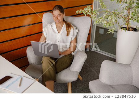 A Professional Young Woman Engaged in Work on a Laptop While in a Modern Office Environment 128847530