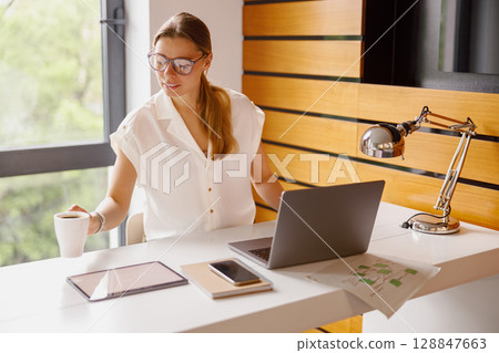 A modern workspace with a professional woman multitasking on devices, focused on productivity 128847663