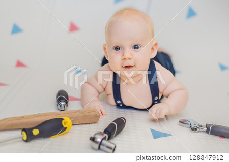 Adorable baby in a mechanic costume surrounded by toy tools. Concept of repair, imaginative play, and introducing kids to the world of fixing and problem-solving through fun 128847912